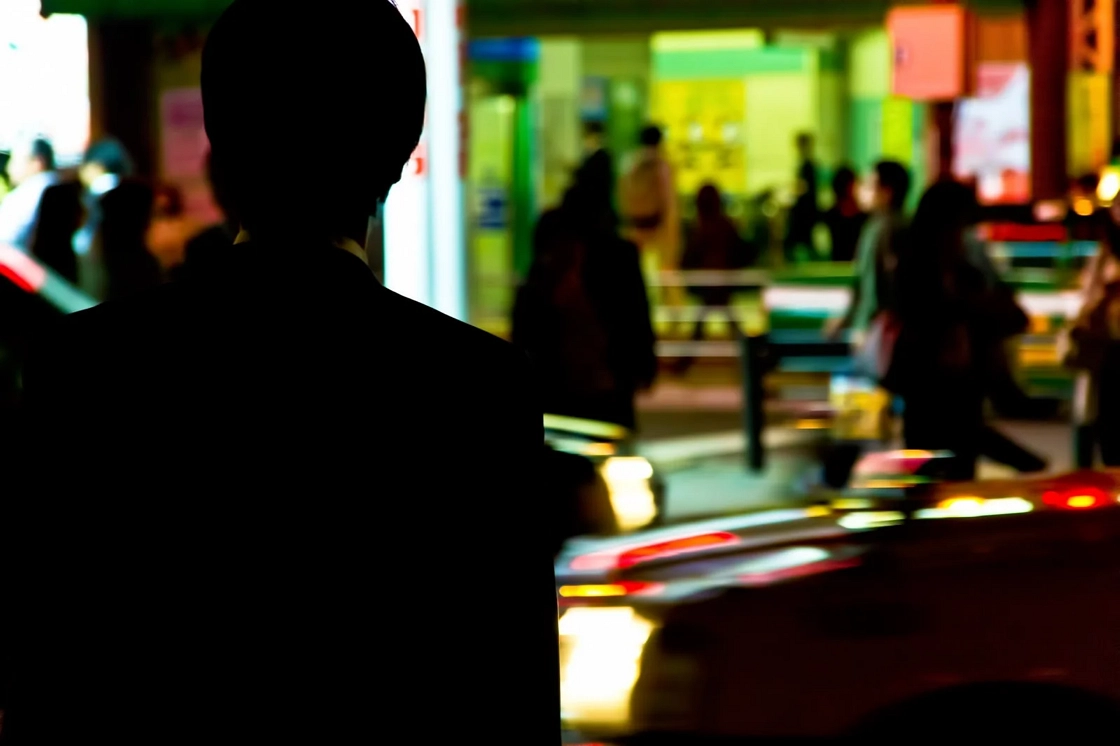 힘든 하루를 마치고 퇴근하는 영포티 회사원의 뒷모습. 주변에는 자동차와 사람들이 빠르게 이동하고 있다.